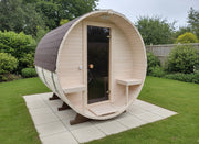Wooden barrel-shaped sauna in a garden setting with greenery around.