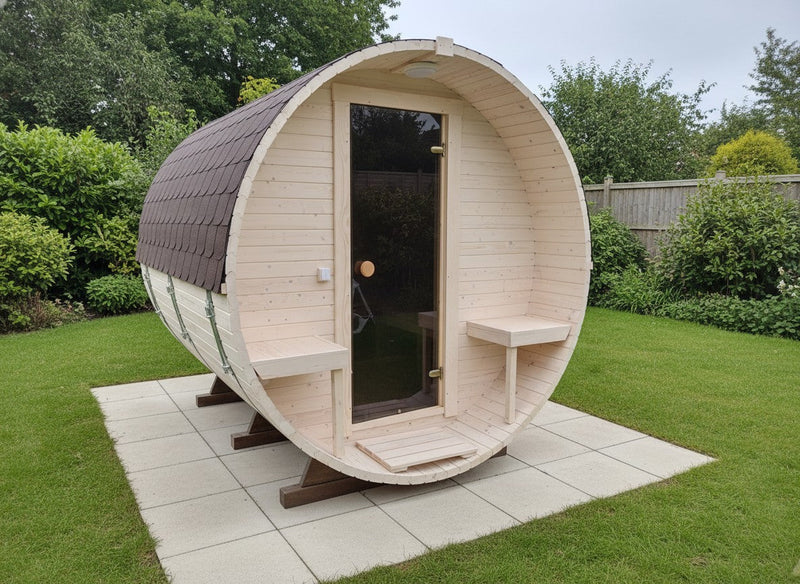 Wooden barrel-shaped sauna in a garden setting with greenery around.